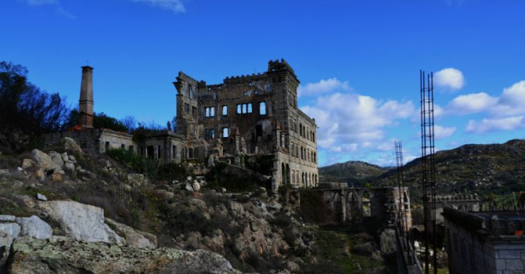 The image shows a spooky place in Guarda. An abandoned and ruined building in the middle fo the picture, on top of rocks and nature surroundings. The building is old and neglected, empty window openings and broken glass.